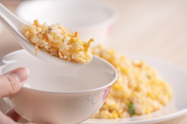 Close up of eating Chinese fried rice with sergestid Sakura shrimp in white plate on bright wooden table surface.