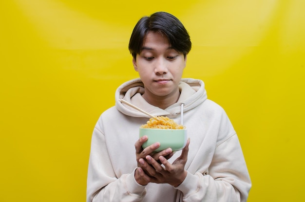 Close-up een Aziatische man in een beige hoodie eet instantnoedels met stokjes en een kom
