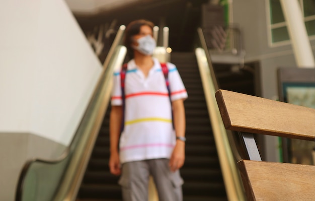 Close-up een houten stoel met onscherpe jonge mens die gezichtsmasker draagt die alleen in een modern gebouw loopt