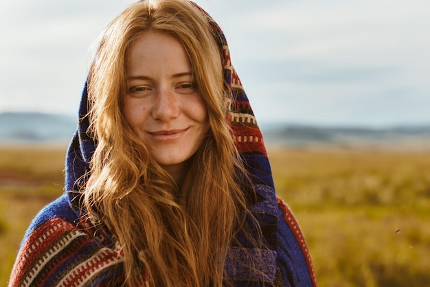 Close-up een meisje met een natuurlijke schoonheid roodharig in een etno cape glimlacht tegen de woestijn steppe