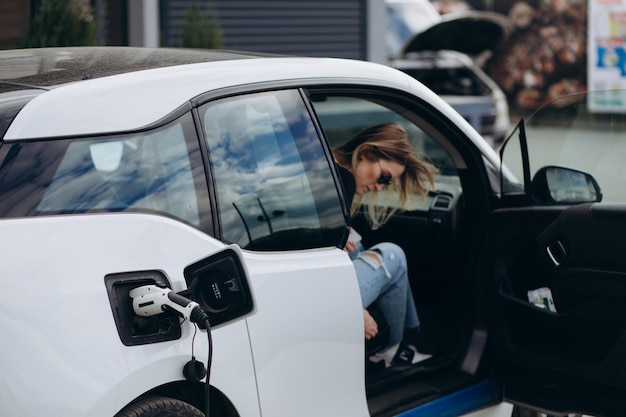 家のドアに入り、車をロックする背景に女性のシルエットを持つ電気自動車充電器のクローズアップ