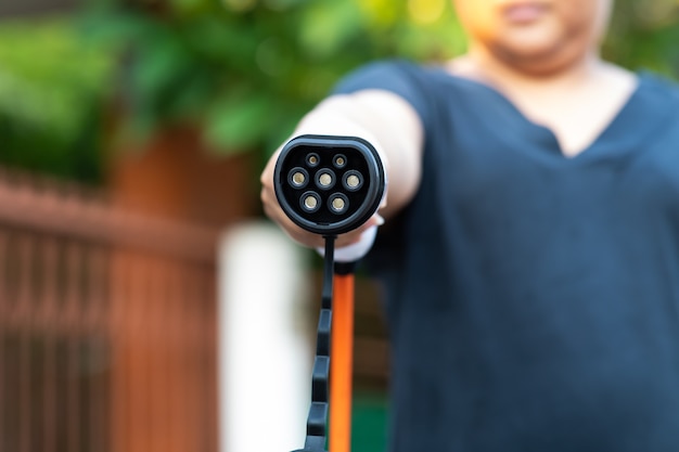 自宅や充電ステーションでハイブリッド車の充電プラグのために電気自動車プラグの女性の手を閉じます。