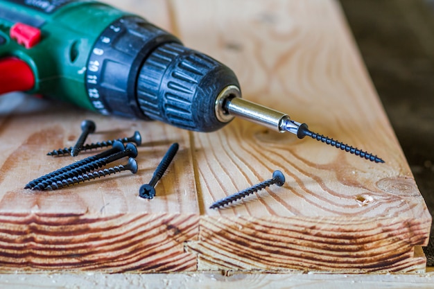 Close up of electric screwdriver with some screws laying on old rough wooden table or vintage natural planks. Building, repairing and home maintenance concept