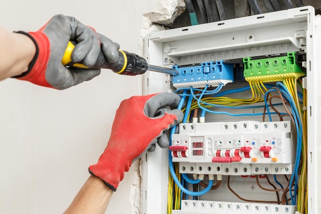 Close up of electrician's hands in working gloves installing and maintainin electrical junction box Electrical services concept