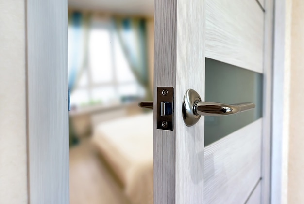 Close-up elements of the interior of the apartment. Ajar white door. Chrome door handle.