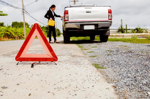 Закройте символ аварийного дорожного предупреждения, чтобы предотвратить дорожные опасности Азиатская женщина, стоящая на заправке грузовика