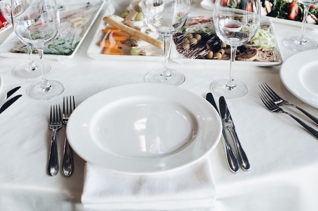 Grande piatto bianco servente vuoto del primo piano circondato dalla forcella del coltello pronta a mangiare l'angolo alto dell'alimento