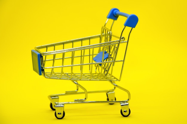 Close-up of empty supermarket metal shopping cart trolley on bright yellow