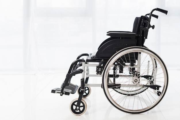 Close-up of an empty wheelchair in a room with white curtain