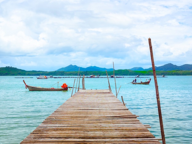 Close up empty wooden pier with local fisherman boats on the sea and sky background in Thailand.