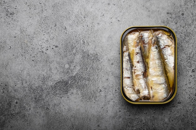 Close-up en bovenaanzicht van ingeblikte sardine in een blikje over grijze betonnen achtergrond, ruimte voor tekst. vis uit blik als gemakkelijke, snelle, gezonde voeding en bron van omega-3 vetzuren, eiwitten en vitamine d