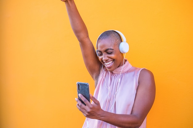 Close-up en portret van een mooie Afro-Amerikaanse vrouw die lacht en plezier heeft met dansen terwijl ze naar muziek luistert met een koptelefoon vanaf haar telefoon - genietend van het gebruik van technologie levensstijl