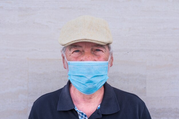 Close-up en portret van een volwassen man en senior die naar de camera kijkt en serieus een medisch en chirurgisch masker draagt om covid-19 of elke vorm van ziekte of griep te voorkomen