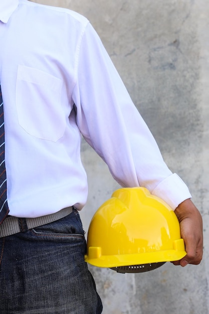 Close up of engineer hand holding a yellow engineer helmet against grey concrete background