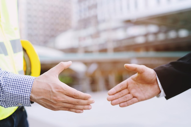Photo close up of a engineering male plan construction project worker hand shake between two business man, represents is good project success approve, congratulations. outdoor of building.