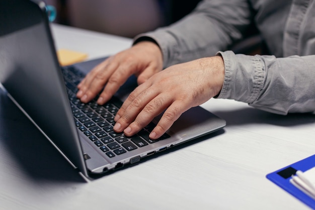 Close up of entrepreneur using laptop computer to finish project. . Male hands typing on laptop keyboard in office. Business, working from home, studying online concept