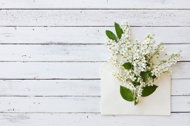 Close-up of envelope with beautiful flowering tree branches on white wooden background.