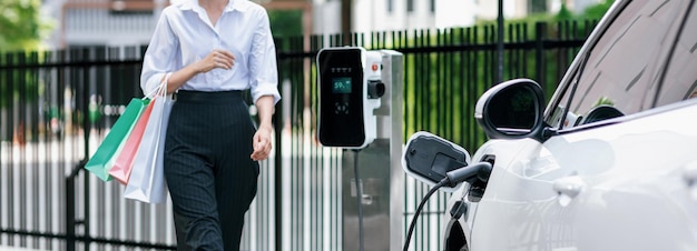 Close-up EV-auto met zakenvrouw die boodschappentas draagt bij laadstation