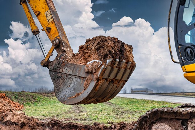 Primo piano della benna dell'escavatore al sito in costruzione l'escavatore sta scavando una trincea per le utenze sotterranee attrezzature da costruzione per lavori di sterro