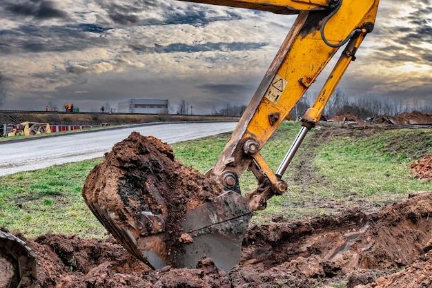 Primo piano della benna dell'escavatore al sito in costruzione l'escavatore sta scavando una trincea per le utenze sotterranee attrezzature da costruzione per lavori di sterro