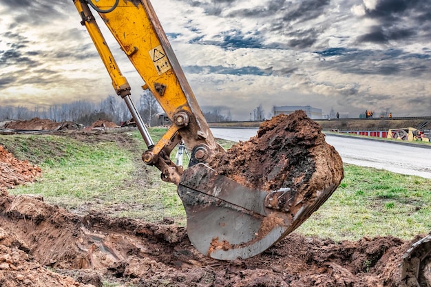 Foto primo piano della benna dell'escavatore al sito in costruzione l'escavatore sta scavando una trincea per le utenze sotterranee attrezzature da costruzione per lavori di sterro