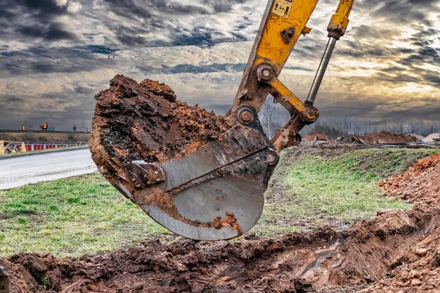 Primo piano della benna dell'escavatore al sito in costruzione l'escavatore sta scavando una trincea per le utenze sotterranee attrezzature da costruzione per lavori di sterro