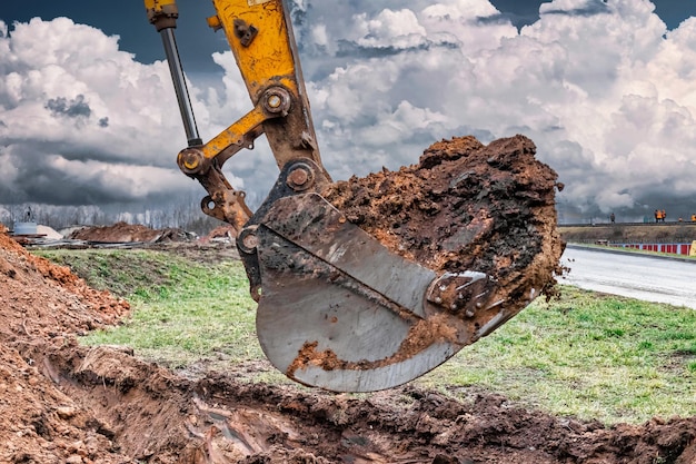 Foto primo piano della benna dell'escavatore al sito in costruzione l'escavatore sta scavando una trincea per le utenze sotterranee attrezzature da costruzione per lavori di sterro