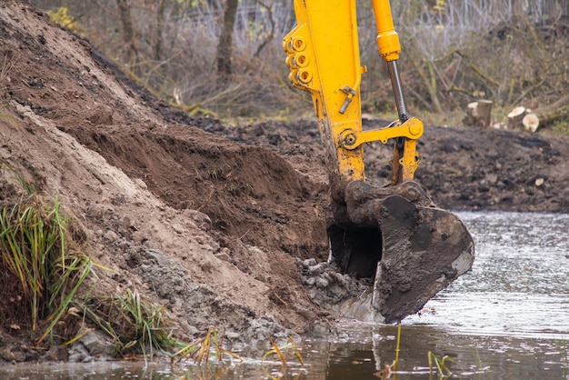 Close up on excavator scoop digging pond in the countryside gradually spreading its size