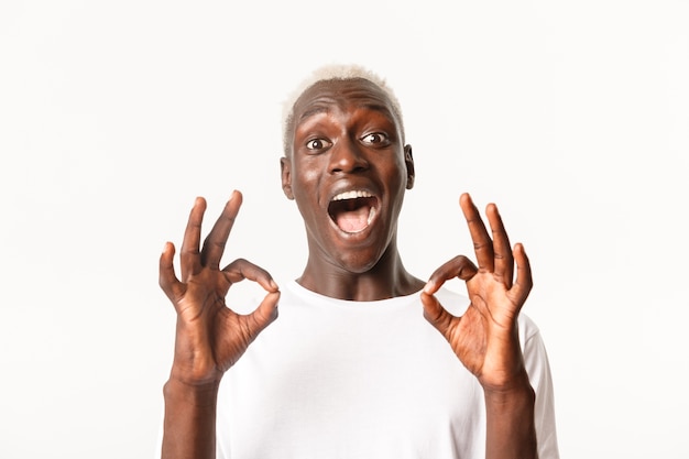 Close-up of excited attractive african-american blond guy express amazement, showing okay gesture in approval