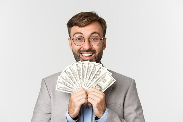 Close-up of excited bearded male entrepreneur in gray suit and glasses, rejoicing and showing big sum of money