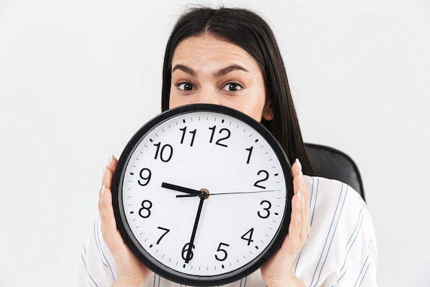 Close up of an excited businesswoman showing alarm clock isolated over white wall