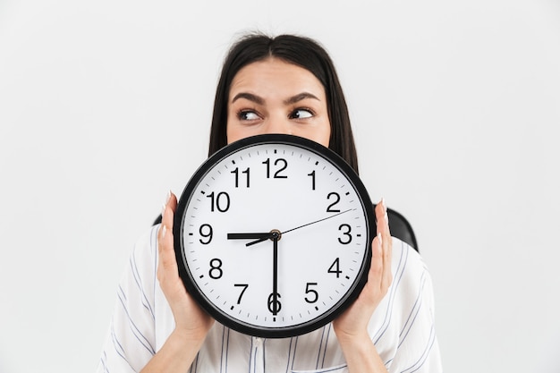 Close up of an excited businesswoman showing alarm clock isolated over white wall