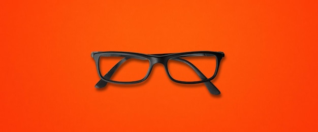 Close-up of eyeglasses on table against orange background