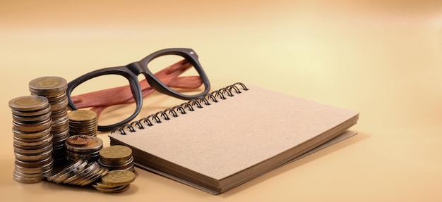 Photo close-up of eyeglasses with coins and spiral notebook on beige background