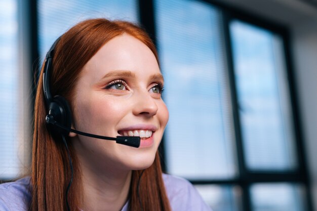 Close-up face of beautiful young woman operator using headset during customer support at home office.