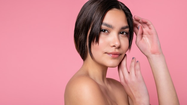 Close up face of beautiful young woman with clean perfect skin. Portrait of beauty model with natural nude make up. Spa, skin care and wellness. Pink peach coral background. 16:9 panoramic format.