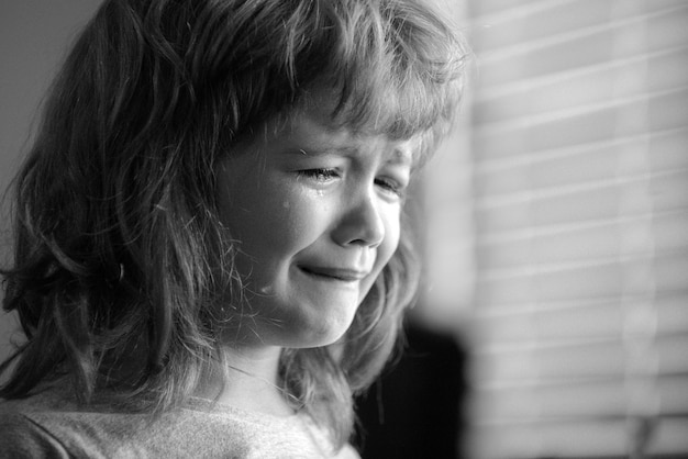 Close up face of crying kid boy sad child with tears at home