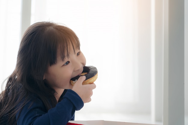 초콜릿 도넛을 먹는 배고픈 작은 아름다운 아시아 여자의 얼굴을 닫습니다, 맛있는 얼굴로 donus를 먹는 귀여운 아이, 아이 eaitng 간식