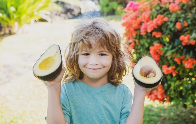 Close up face of kid with half an avocado in her hand next to her lies a whole avocado Healthy kids concept