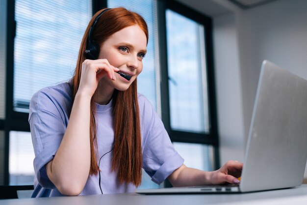 Close-up face of pretty young woman operator using headset and laptop during customer support at home office.