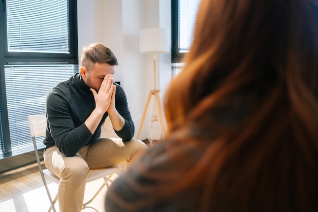 Photo close-up face of upset desperate young man sharing problem sitting in circle during group interpersonal therapy session. sad depressed male talking with compassionate patients and psychotherapist.