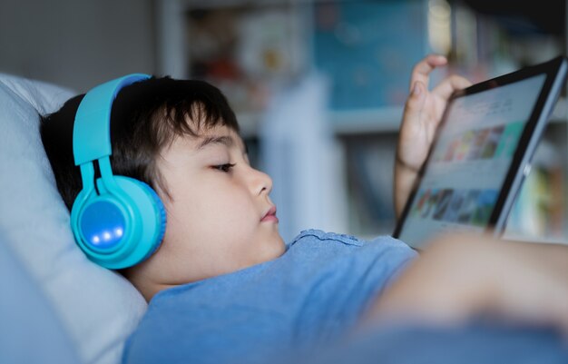 Close up face young boy wear wireless headphone listening music while sitting in bed