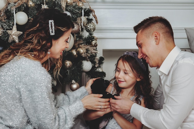 Close-up familie met schattig hondje in de woonkamer bij gezellig huis Familie sfeervol moment bij gouden mooie kerstboom