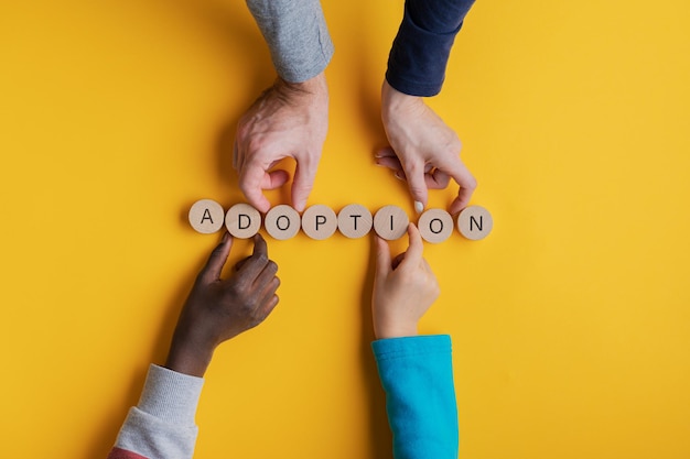 Photo close-up of family hands arranging adoption text on yellow background