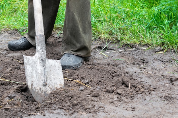 Close up of farmer digging soil with shovel in rubber boots