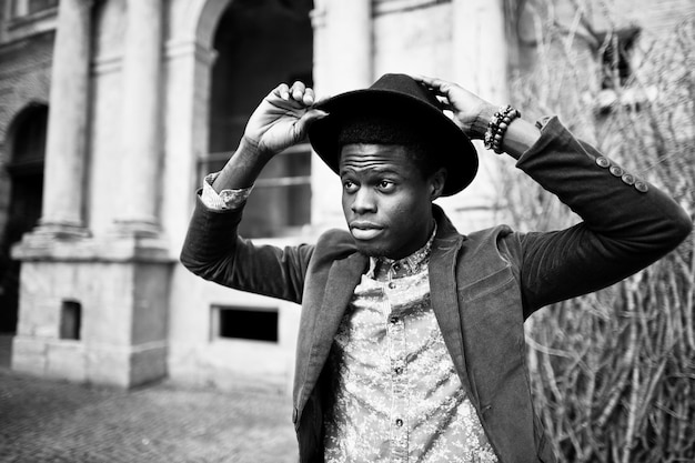 Close up fashion portrait of black african american man on green velvet jacket and black hat background old vintage house with arch and columns BW photo