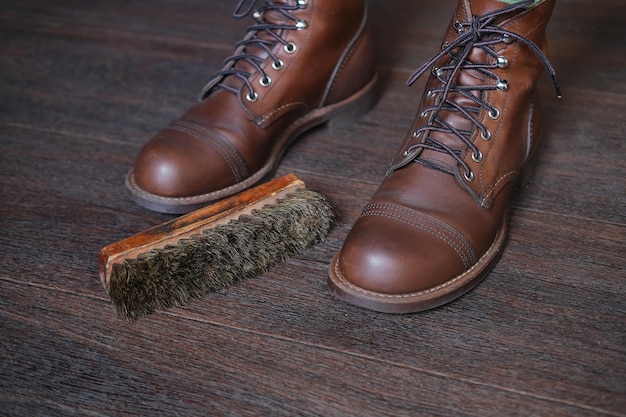 靴ブラシの横にある木製の床にファッションのラフ レザー メンズ ブーツのクローズ アップ