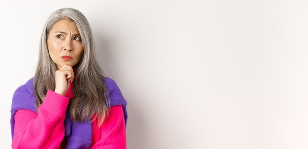 Close up of fashionable asian mature woman with grey hair thinking and looking serious looking person