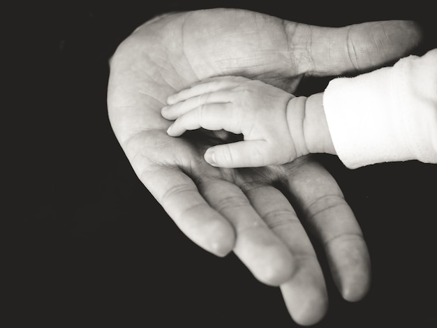 Photo close-up of father holding hand of baby against black background