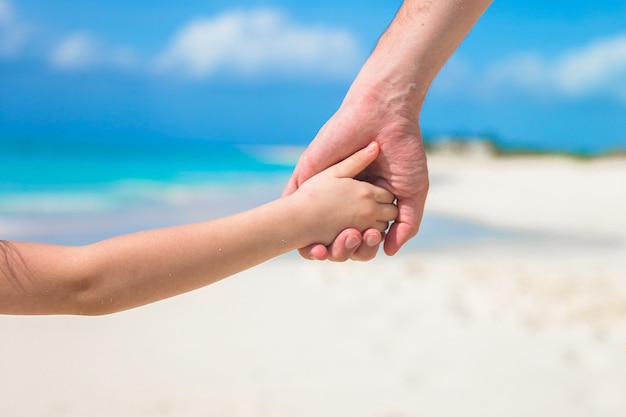 Close up of father and little kid holding each other hands at beach